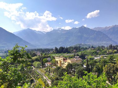 Meran (Merano), Güney Tyrol, İtalya 2 Mayıs 2025: Trauttmansdorff Kalesi 'nin bahçeleri ve arka plandaki alp manzarası üzerine panoramik manzara. Baharda güneşli bir gün. 