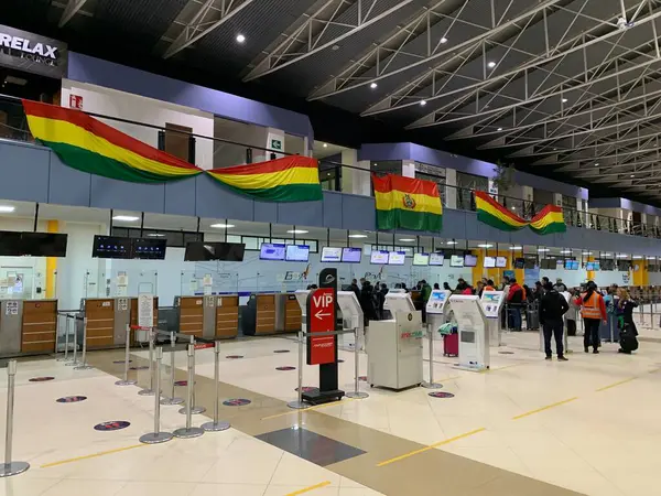 La Paz, Bolivya - 02 Haziran 2025: Yolcular El Alto Uluslararası Havaalanı SLLP 'nin kalkış salonundaki bavullarını kontrol ediyorlar. Renkli Bolivya bayrakları yolcuları karşılıyor.