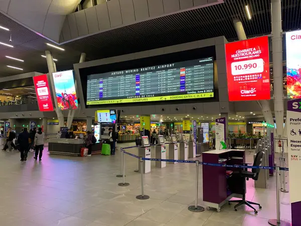 Santiago, Şili - 8 Haziran 2025: Arturo Merino Bentez Uluslararası Havalimanı SCEL 'de CUSS self-servis büfesi ile kontrol bölgesi. Yukarıdan aydınlatılmış Uçuş Bilgileri Görünüm Sistemi FIDS. 