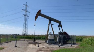 Gaenserndorf, Aşağı Avusturya - 11 Ağustos 2025: Eski paslı petrol pompacısı, yoğun olarak kullanılan verimli tarım arazileri, rüzgar türbinleri ve elektrik pilonlarından etkilenen insanların yaşadığı bir yer..