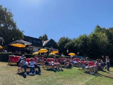 Viyana, Avusturya - 24 Ağustos 2025: Geleneksel Viyana şarap üreticisi festivali Neustifter Kirtag ziyaretçileri arka planda şarap tavernası Zeiler tarafından sunulan şezlonglarda dinleniyor. Eğimli arazi, sarı güneş gözlüğü.