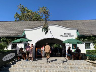 Viyana, Avusturya - 24 Ağustos 2025: Şarap tavernası Weingut Fuhrgassl-Huber 'a çam ağacından yapılmış giriş kapısı açık olduklarını gösteriyor. Geleneksel kıyafetler giyen ziyaretçiler. Ausg 'steckt!