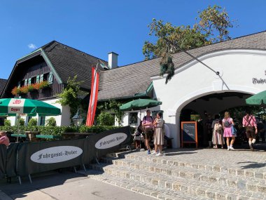 Viyana, Avusturya - 24 Ağustos 2025: Şarap tavernası Weingut Fuhrgassl-Huber 'a çam ağacından yapılmış giriş kapısı açık olduklarını gösteriyor. Geleneksel kıyafetler giyen ziyaretçiler. Ausg 'steckt!