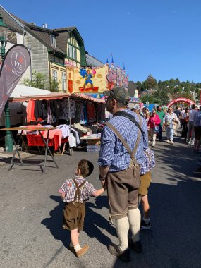 Viyana, Avusturya - 24 Ağustos 2025: Baba oğullarını her iki tarafta da tutuyor, hepsi geleneksel Lederhosen ve damalı gömlekler giyiyor. Geleneksel Viyana şarap üreticisi festivali Neustifter Kirtag.