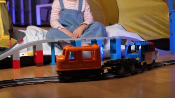 テントで鉄道や電車で遊んでいる少女の肖像画 面白い幼い女の子は 自宅の床にプラスチック製のレールを接続する玩具列車で遊んでいます かわいい赤ん坊の子供 高品質の4K映像 — ストック動画