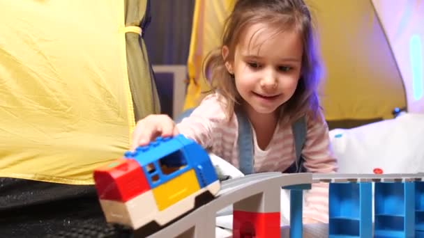 テントで鉄道や電車をやっているかわいい女の子 面白い幼い女の子は 自宅の床にプラスチック製のレールを接続する玩具列車で遊んでいます かわいい赤ん坊の子供 高品質の4K映像 — ストック動画
