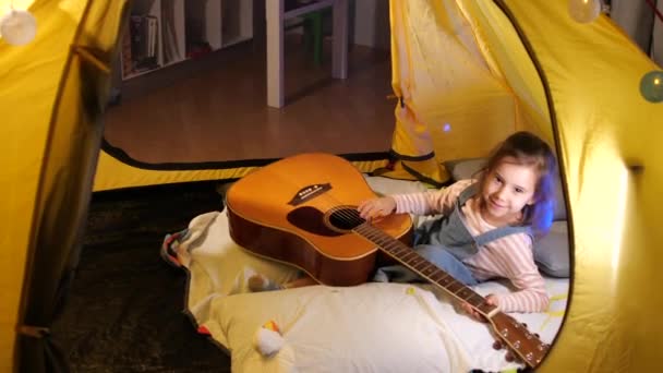 小屋の家でギターを弾く少女 テント 少女はギターを弾くことを学ぶ 初めてギターを弾こうとする 4K映像について — ストック動画