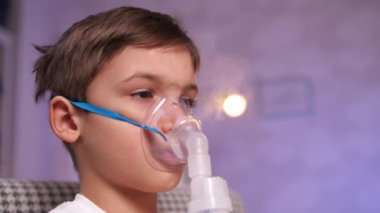 Nebulizör maskeli bir çocuğun portresi, evde grip, bronşit, astım tedavisi gören bir astım spreyi. Evde tedavi. Küçük bir çocuk öksürük ve bronşit sırasında solunum maskesiyle oturur..
