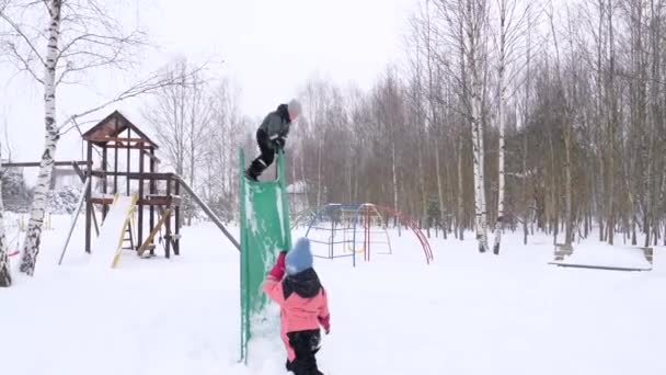 一个男孩从小孩身上跳下滑向雪地 滑向雪地 孩子们的操场被雪覆盖着 — 图库视频影像