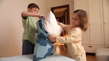 Oğlan ve kız çarşafları değiştirip yatağı yapıyorlar. Çocuklar ev işlerinde ebeveynlerine yardım ederler. Bir oğlan ve küçük bir kız birbirlerine yardım ediyorlar. Abim ve ablam ev işlerini birlikte yapıyorlar..