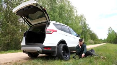 The man want to replace a flat tire with a spare tire. The driver calls the car repair service. male driver sitting near a broken car, emergency stop on the side of the road