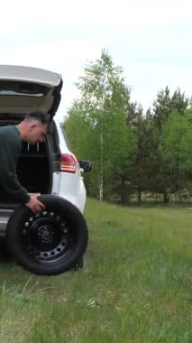 Yol kenarındaki bir arabanın patlak lastiğini değiştiren dikey bir video. Şoförün kendisi patlak lastiği yedek lastikle değiştiriyor. Şoför arabanın bagajındaki yedek lastiği çıkardı.