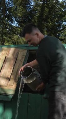 Bir adam eski bir köy kuyusundan el yapımı içme suyu alıyor. Bir adam kovayı kuyudan tatlı suyla doldurur.