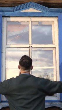 Dikey videoda bir adam eski ahşap bir evin penceresinin kepenklerini kapatır. Belarus kırsalındaki bir evin ahşap kepenklerini kapatmak. Doğu Avrupa 'daki kır evi