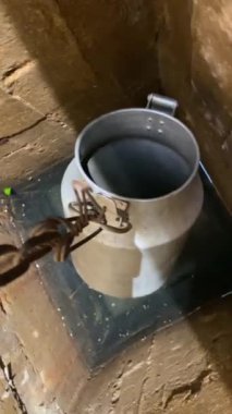 Dikey video bir kovayı zincire geçirir ve su kuyusuna indirir. Bir kova eski bir kuyudan su çeker.