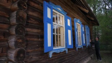 Bitiriş ve bitiş konsepti. Pencereyi kapatıyorum. Bir adam penceredeki ahşap panjurları kapatır. Belarus 'taki eski ahşap kırsal ev