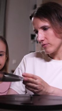 Dikey video anne ve küçük kızı klasik bir pikapta müzik dinliyorlar. Küçük bir kız müziği açar. Anne ve kızı birlikte vakit geçiriyorlar. Mutlu bir aile..