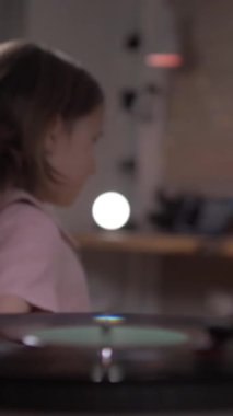 düşey video kaydı oynatıcıda dönüyor. Kız müziği açtı. Küçük kız evde vinil plak çalar sesiyle dans ediyor. Küçük bir kız müziği açar ve dans etmeye başlar. 