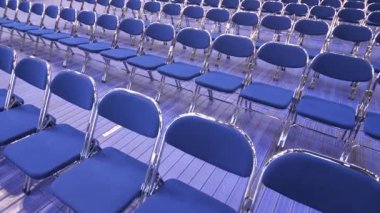 Seminerden önce boş oditoryum, konser, ön seçimler, tartışmalar. Seyircisi olmayan boş mavi sandalyeler. Geçici seyirci koltukları. Metal katlanır sandalyeler