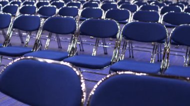 Boş mavi koltuklara yakın çekim. Seminerden, konserden, ön seçimlerden önce izleyicisi olmayan boş mavi sandalyeler. Geçici seyirci koltukları. Metal katlanır sandalyeler. kamera hareketleri