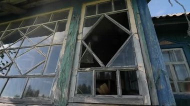 Terk edilmiş bir köy evinde kırık bir pencere. Terk edilmiş eski bir ahşap çiftlik evi çürüyor ve dökülüyor, çalılar ve otlarla kaplanıyor. Ev yabani çalılarla kaplanmış.. 