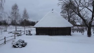 Köydeki eski ahşap bina. Karda sazdan çatılı bir ahır. Doğu Avrupa, Ukrayna ya da Belarus 'ta bir köy. Kışın şafak vakti köyde. İHA videosu, hava görüntüsü. Elektrik yok.