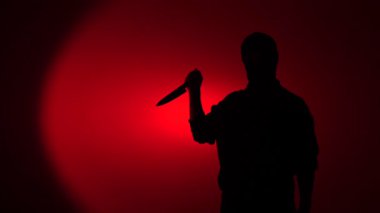 Silhouette of a menacing man with a knife against a stark red background, evoking crime, danger and psychological thriller tension in a dark, dramatic studio composition