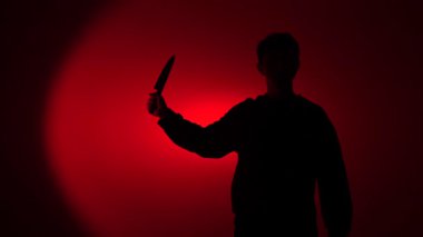 Mans dark silhouette lifts a large kitchen knife against a blood red background, evoking threat, violence, horror and anonymous menace for crime, thriller and suspense themes