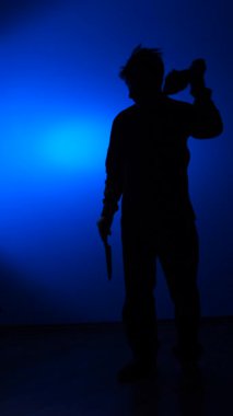 vertical video A silhouette of a man wearing a balaclava and holding a knife. The man removes the balaclava and shakes his head in disappointment. Concept of fatigue. Concept of a repentant criminal. Robber.