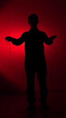 vertical video Person silhouette standing in a red spotlight, holding a rosary and creating a scene full of mystery and introspection, embodying themes of faith and inner reflection