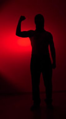 Vertical video silhouette of a man flexing his bicep against a dramatic red background, symbolizing concepts of strength, determination, power, and success in a dynamic way