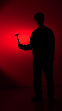 vertical video Silhouette of a man standing against a bright red background, holding a hammer in his hand, conveying themes of danger, crime, violence, and intimidation
