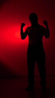 Vertical video silhouette of a powerful man standing with clenched fists, embodying strength, determination, and intense emotion against a dramatic red lit background