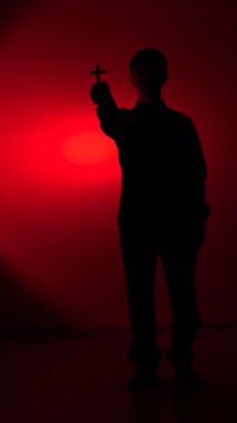 vertical video Persons dark silhouette holding a cross against a dramatic red background, symbolizing faith, protection, and the spiritual battle against dark forces