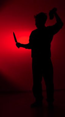 vertical video A silhouette of a man wearing a balaclava and holding a knife. The man removes the balaclava and shakes his head in disappointment. Concept of fatigue. Concept of a repentant criminal. Robber.