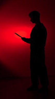 vertical video Silhouette of man holding a pipe wrench against a red backlight, evoking danger, mystery and hidden threat in a dramatic, industrial style studio shot