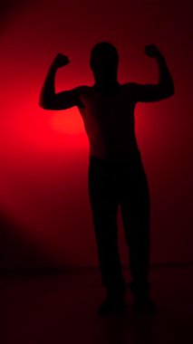 Vertical video fighter man in silhouette stands flexing his biceps, symbolizing strength, determination, and power against a vibrant red backdrop, representing energy and passion