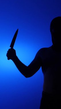 Arka planda büyük bir bıçak tutan tehditkar bir adamın dikey video silueti, dramatik mavi arka plan, tehdit, korku ve şiddet, şüpheli, gizemli suç mahalli