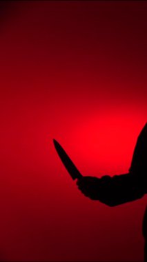 Dikey videocuların koyu renk silueti, canlı kırmızı bir arkaplan üzerinde keskin bir bıçak taşıyor, tehlike, suç, şiddet ve belirsizlik hissi uyandırıyor.