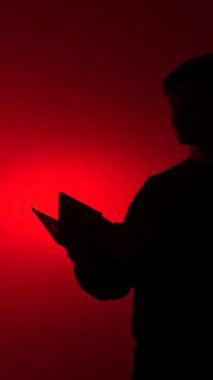 vertical video Person silhouette standing, intently reading a book with pages turning, bathed in a dramatic spot of red light offering a sense of mystery, learning, and storytelling