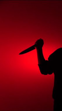 Dikey video, elinde keskin bir bıçak tutan bir kişi dramatik, uğursuz bir kırmızı arka plan, tehlike, suç, korku ve şiddet kavramları taşır