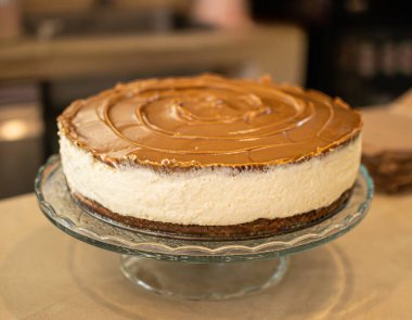 Yumuşak karamel kaplamalı kremalı cheesecake 'in yakın çekimi. Zarif bir cam pasta standına yerleştirilmiş. Sanatsal vejetaryen hamur işi kavramı. Küçük işletmeler