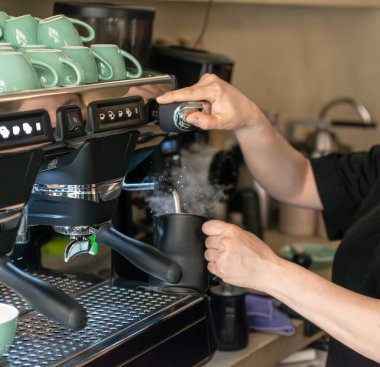 Tanınmayan bir barista, küçük bir kahve dükkanı var. Profesyonel espresso makinesi kullanarak bitki sütü ısıtıyor ve köpürüyor. Sütsüz kahve içeceği hazırlarken buhar yükseliyor. Sahne