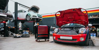 Birçok aracın bakım için çalındığı yoğun bir araba tamir atölyesinin içinde. Açık kaputlar, taşınabilir araç tablosu ve parçalar mekanik çalışma ve otomotiv hizmeti için endüstriyel bir sahne oluşturur.