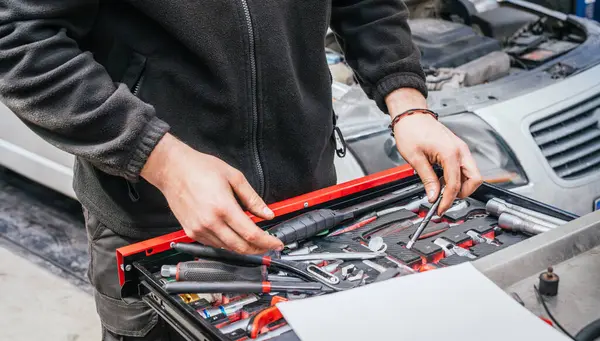 Tanımlanamayan erkek tamirci, arka planda açık araba kaputu olan organize çekmeceden profesyonel bir atölyede tamir görevi için araç seçiyor..