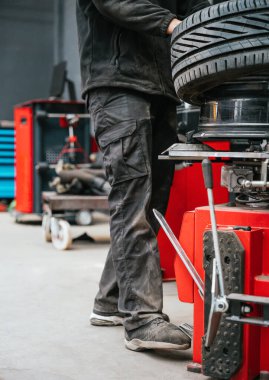 Tekerlek değiştirme makinesinin pedalına basan bir mekaniğin yakın çekimi. Tekerlek bakımı sırasında fiziksel iş gücü, atölye etkinliği ve ekipman denetimini vurgular.
