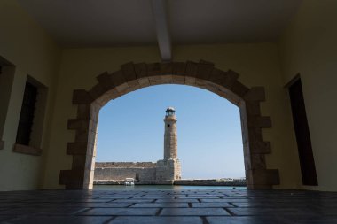 Arka planda mavi gökyüzü olan taştan bir kemer yolunda bir deniz feneri, Rethymno, Girit Adası, Yunanistan