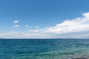 Mavi gökyüzü ve su kütlesi olan bir sahil.