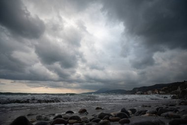 Kayaları ve bulutlu gökyüzü olan bir sahil.