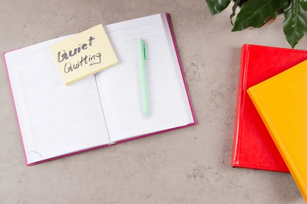 Workplace desk with paper business notebook planner with sticky note and text Quiet Quitting on it. Work-to-rule, in which employees engage in work related activities solely within defined work hours.